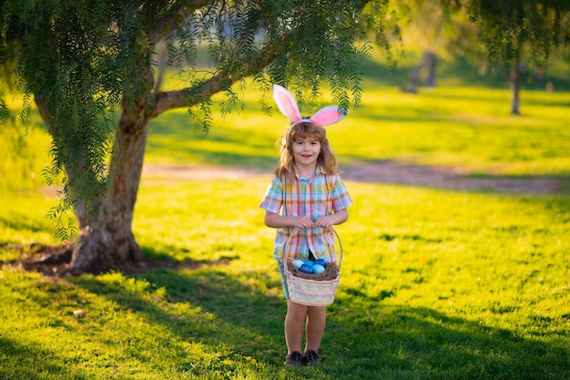 Мальчик-кролик в костюме кролика с кроличьими ушами охотится за пасхальными яйцами в парке