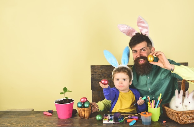 Orecchie da coniglio e orecchie da coniglio disegnano padre e figlio che dipingono le uova di pasqua