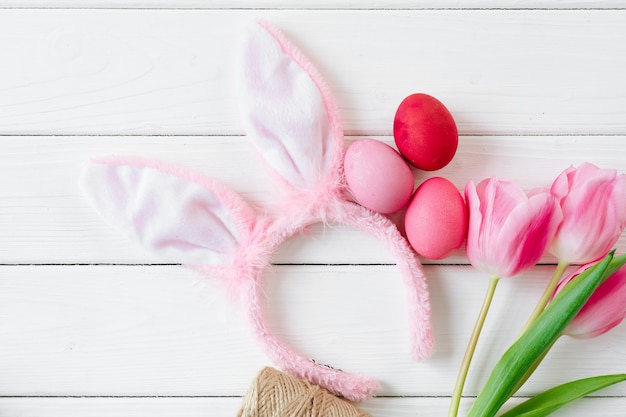 Bunny ears with tulips and colored eggs on wooden background flat lay