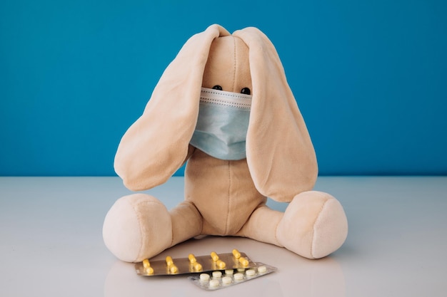 Bunny speelgoed in masker met pillen op een blauwe achtergrond Kinderziektes concept