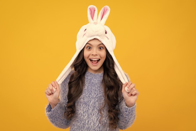 Bunny winter hat Amazed teenager Modern teenage girl 12 13 14 year old wearing sweater and knitted hat on isolated yellow background Excited teen girl