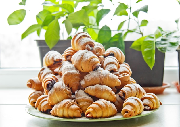 Buns in a plate full of freshly baked bagels sprinkled with powdered sugar on the kitchen table cooking baking croissants baking preparation stage breakfast closeup copy space