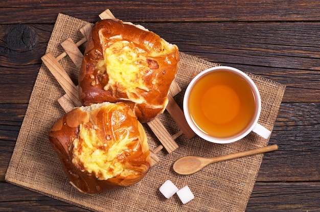 Buns with cheese and cup of tea on dark wooden table, top view