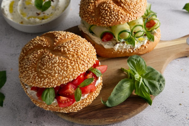 Buns with sesame seeds, cheese cream and fresh tomatoes, cucumbers and with basil leaves close up