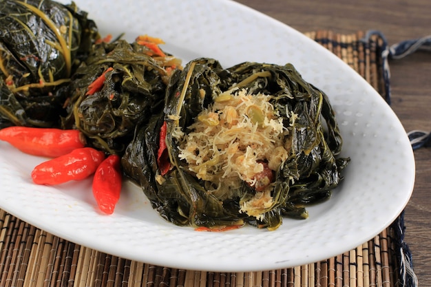 Photo buntil is traditional indonesian food made from papaya/cassava leaves stuffed with grated coconut, petai cina,  and anchovy fish. popular in javanese and sundanese cuisine, copy space isolated