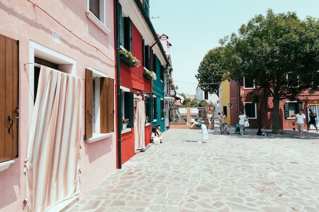 Burano, Venice, Italy - July 2, 2018: Panoramic view of brightly coloured homes of Burano is an island in the Venetian Lagoon. People walk and rest on streets. Summer sunny day and blue sky