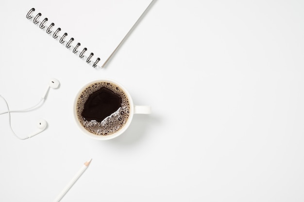 Bureau bovenaanzicht met koffiekopje, notebook en hoofdtelefoon op witte achtergrond.