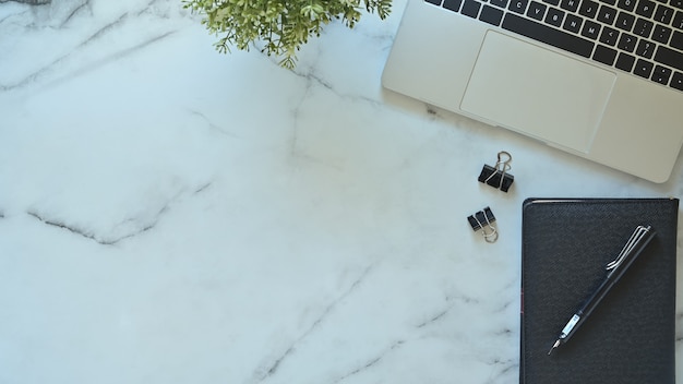 Bureau laptop, pen en notitieblok met plant op marmeren tafel met bovenaanzicht