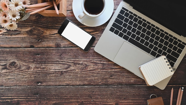 Bureau laptop, smartphone en kantoorbenodigdheden met koffie, bovenaanzicht werkruimte oude houten tafel.