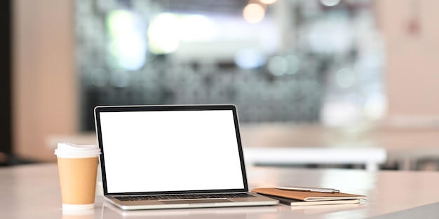 Bureau met geïsoleerde scherm laptopcomputer, koffie en notebookpapier op witte tafel.