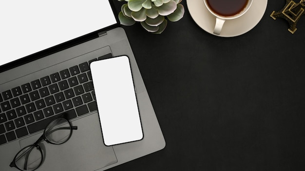 Bureau met laptop computer smartphone wit scherm mockup en kopieer ruimte op zwarte achtergrond