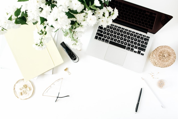 Bureau werkruimte met laptop, bloemen boeket en briefpapier op witte tafel