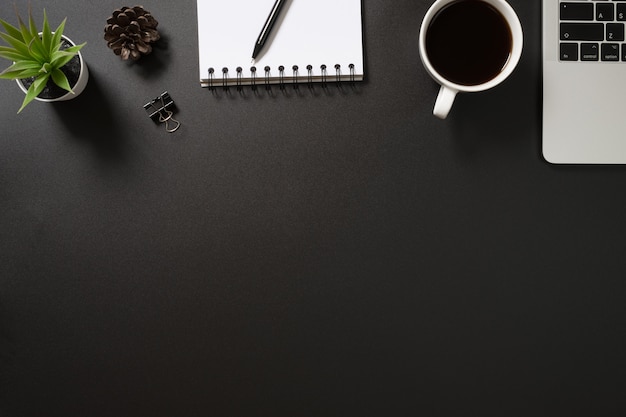 Bureaukantoor bovenaanzicht met computer, pen, Kladblok, koffie en plant op zwarte achtergrond.