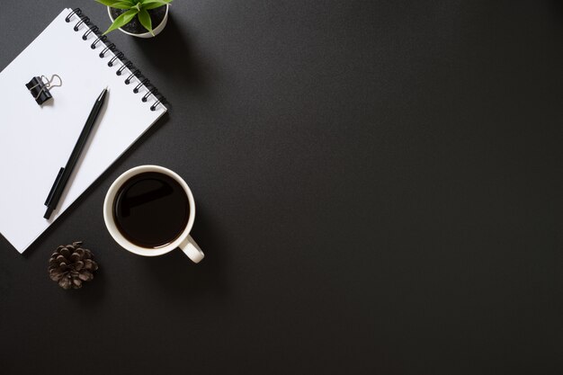 Bureaukantoor bovenaanzicht met lege Kladblok, pen, koffie en plant op zwarte achtergrond.