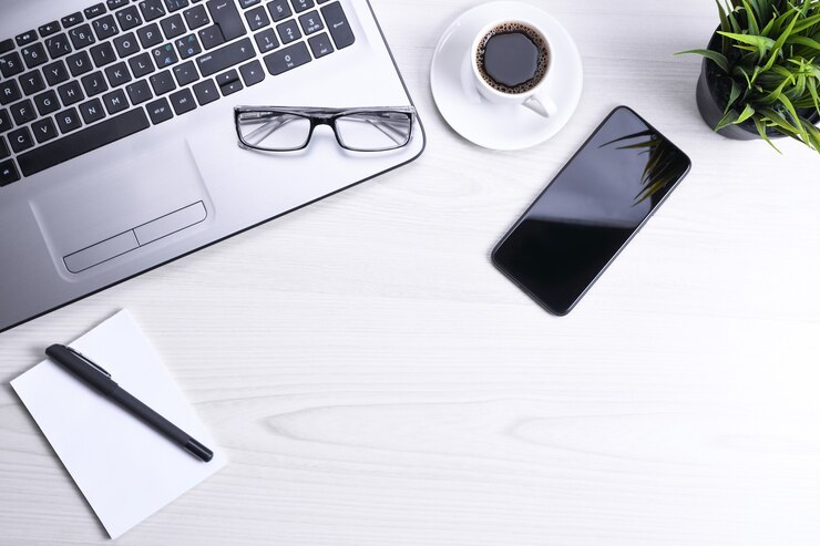 Foto bureautafel met laptop, slimme telefoon, kopje koffie en benodigdheden, op houten