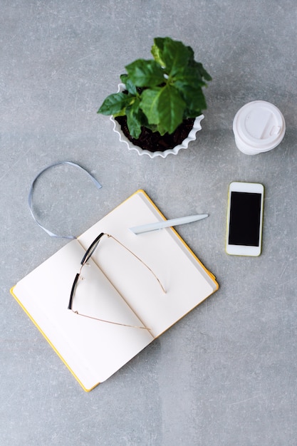 Bureautafel met notebookplanner, smartphone, bril, koffieboom en koffiekopje.