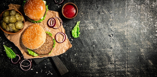 Burger on a cutting board with onion rings tomato sauce and lettuce