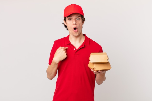 Burger deliver man looking shocked and surprised with mouth wide open, pointing to self