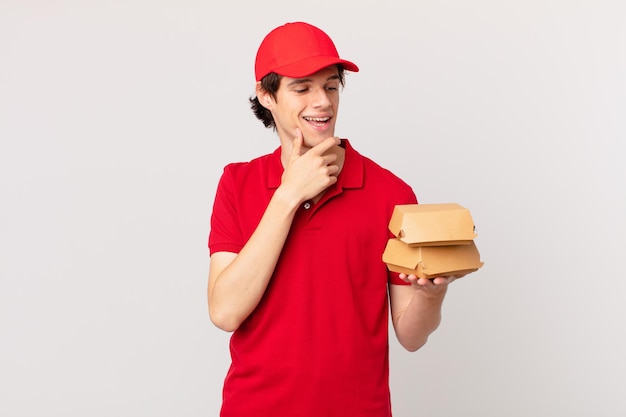 Burger deliver man smiling with a happy, confident expression with hand on chin
