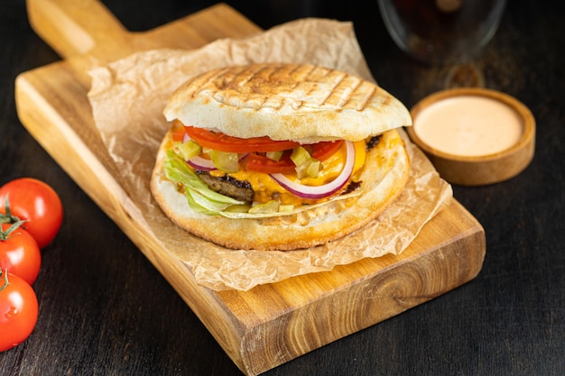 Burger in pita breads with grilled meat vegetables and sauce on dark background banner menu recipe