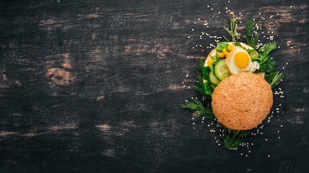 Сэндвич с бургером с перепелиным яйцом, огурцом и кукурузой на деревянном фоне Вид сверху Копией пространства