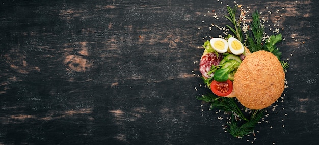 Burger sandwich with salami quail eggs and cherry tomatoes On a wooden background Top view Copy space