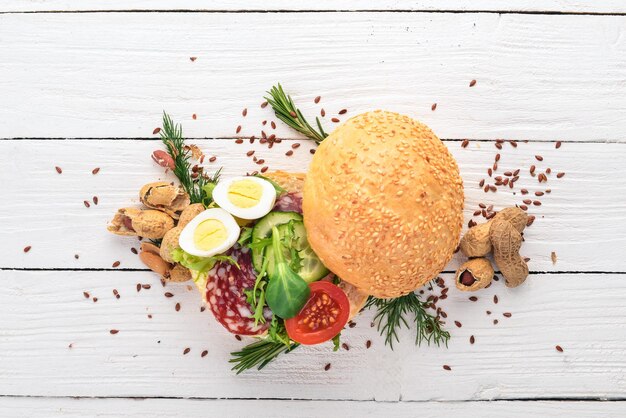 Burger sandwich with salami quail eggs and cherry tomatoes On a wooden background Top view Copy space