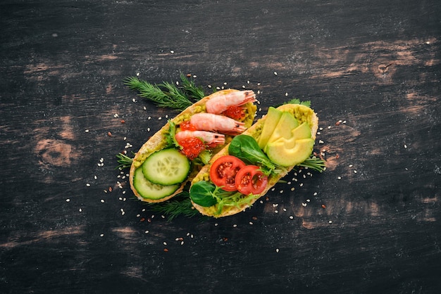 Burger sandwich with shrimp avocado caviar and cucumber On a wooden background Top view Copy space