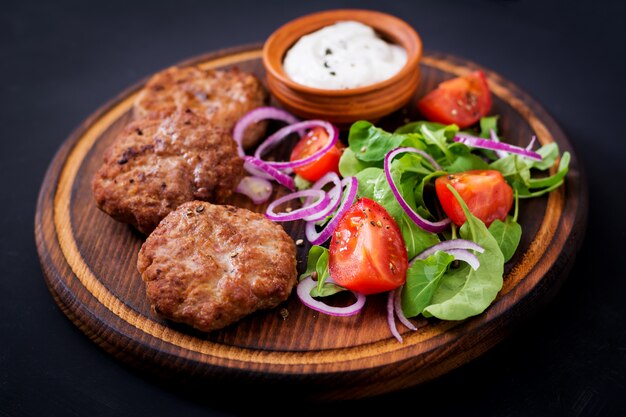 burger and tomato with basil and herbs on a brown plate