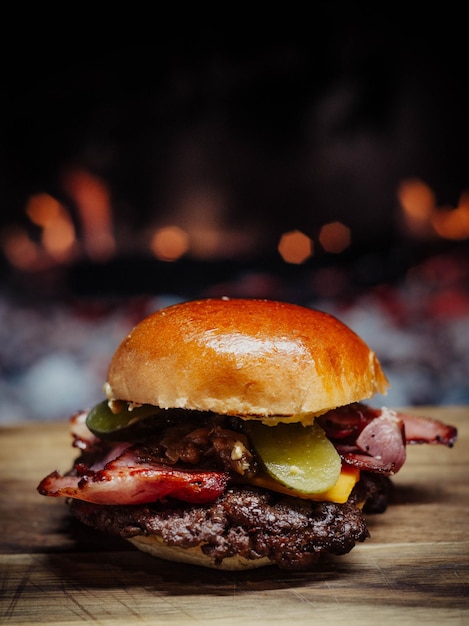 A burger with bacon and cheese on it sits on a wooden table in front of a fireplace.