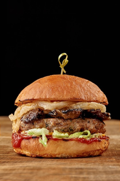 Burger with bacon meat tomato and lettuce on wooden background close up