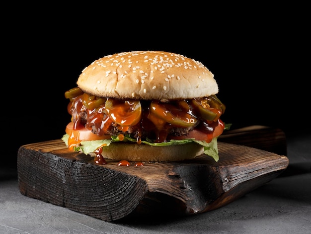 Burger with bacon meat tomato and lettuce on wooden board and black background Close up