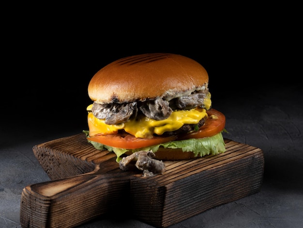 Burger with bacon meat tomato and lettuce on wooden board and black background Close up