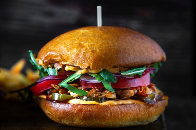 Burger with chicken teriyaki, tomatoes and arugula on a wooden board