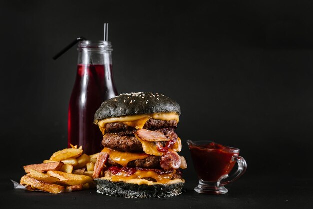 A burger with french fries, tomatoe sauce and glass of juice on the black background