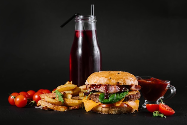 A burger with french fries, tomatoe sauce and glass of juice on the black background