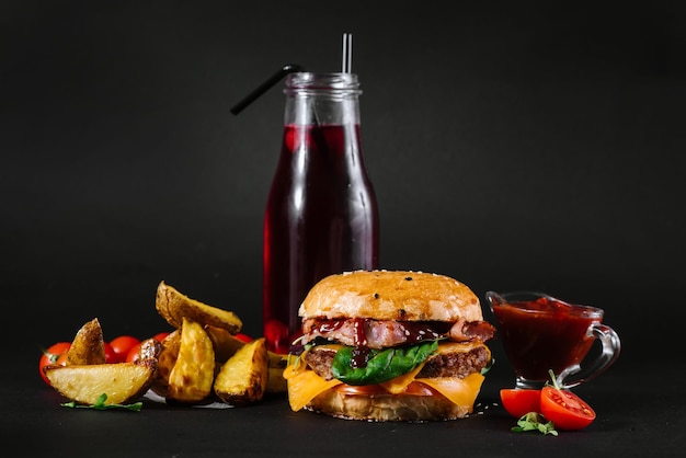 A burger with french fries, tomatoe sauce and glass of juice on the black background