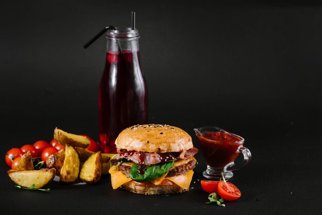 A burger with french fries, tomatoe sauce and glass of juice on the black background