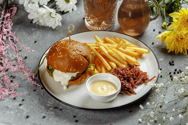 Burger with fries and sauce on a white plate.