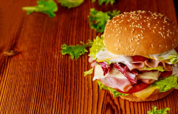 Burger with lettuce, cheese, ham and tomato on dark background. Close up.