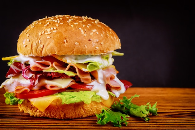 Burger with lettuce, cheese, ham and tomato on dark surface