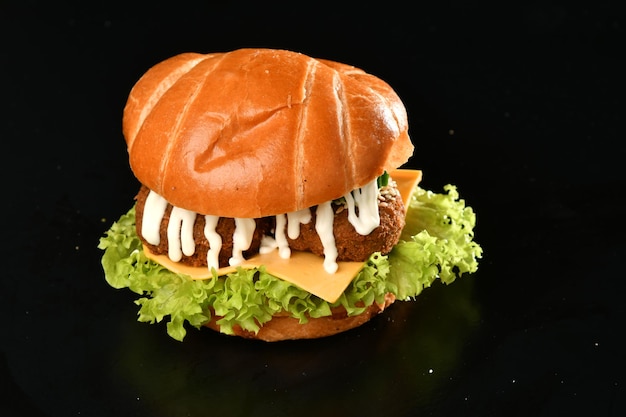 A burger with mayo on it sits on a black table.