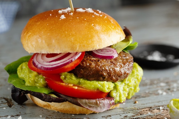 Burger with meat and avocado sauce served on wooden table. Closeup.