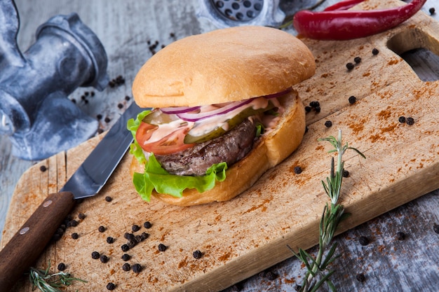 burger on wooden board with knife and grinder with pepper