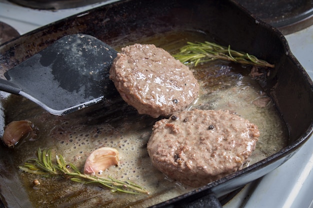 The burgers are fried in a pan with rosemary and garlic.