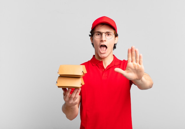 Burgers deliver boy looking serious, stern, displeased and angry showing open palm making stop gesture