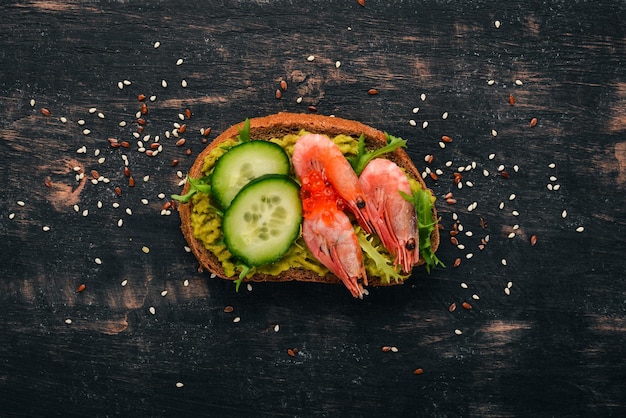 Burgersandwich met garnalen, avocado-kaviaar en komkommer Op een houten ondergrond Bovenaanzicht Kopieer de ruimte