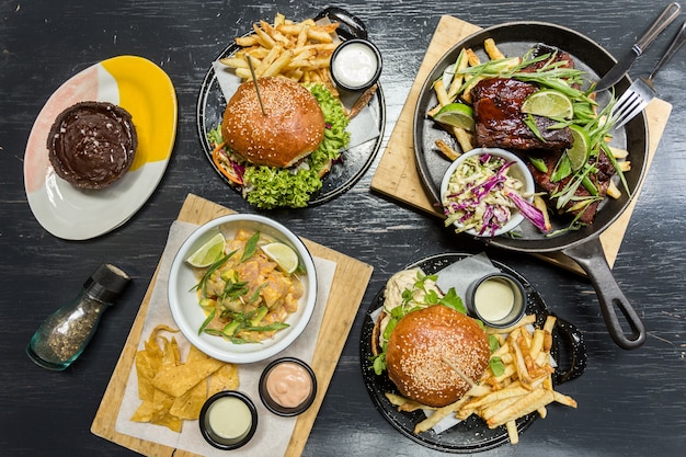 Burgersm frietjes, ceviche, ribben en muffin op een houten tafel