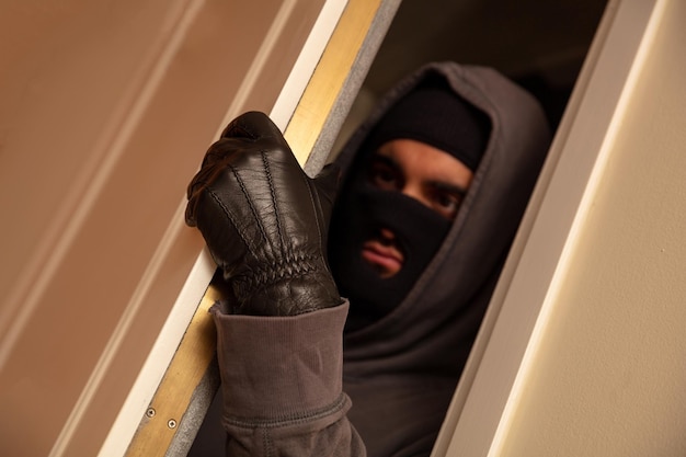 Photo burglar in black balaclava entering the house housebreaking burglary concept