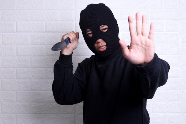 写真 目出し帽をかぶった強盗の男がナイフを持ち、手のひらを見せている